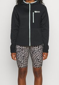 Svart zip-up hoodie med en ljusblå dragkedja och luva, i kombination med cykelbyxor i leopardmönster i beige och svart.