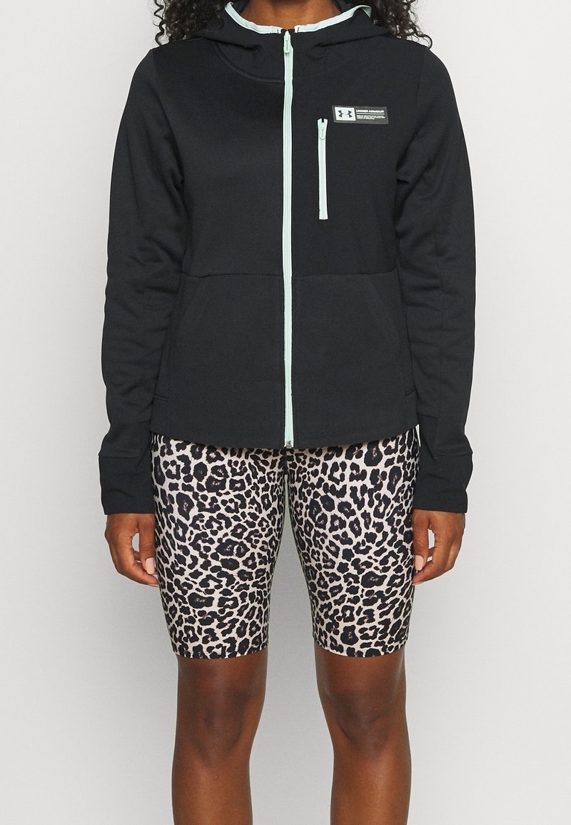 Svart zip-up hoodie med en ljusblå dragkedja och luva, i kombination med cykelbyxor i leopardmönster i beige och svart.