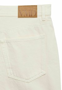 Poche arrière d'un jean en denim couleur crème avec une étiquette en cuir cousue affichant "VMD" à la ceinture.