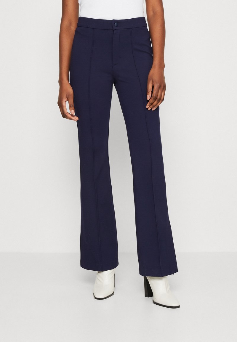 Pantalon évasé bleu marine avec une texture lisse, doté d'une fermeture à boutons sur le devant, de poches latérales et de détails de coutures en contraste.