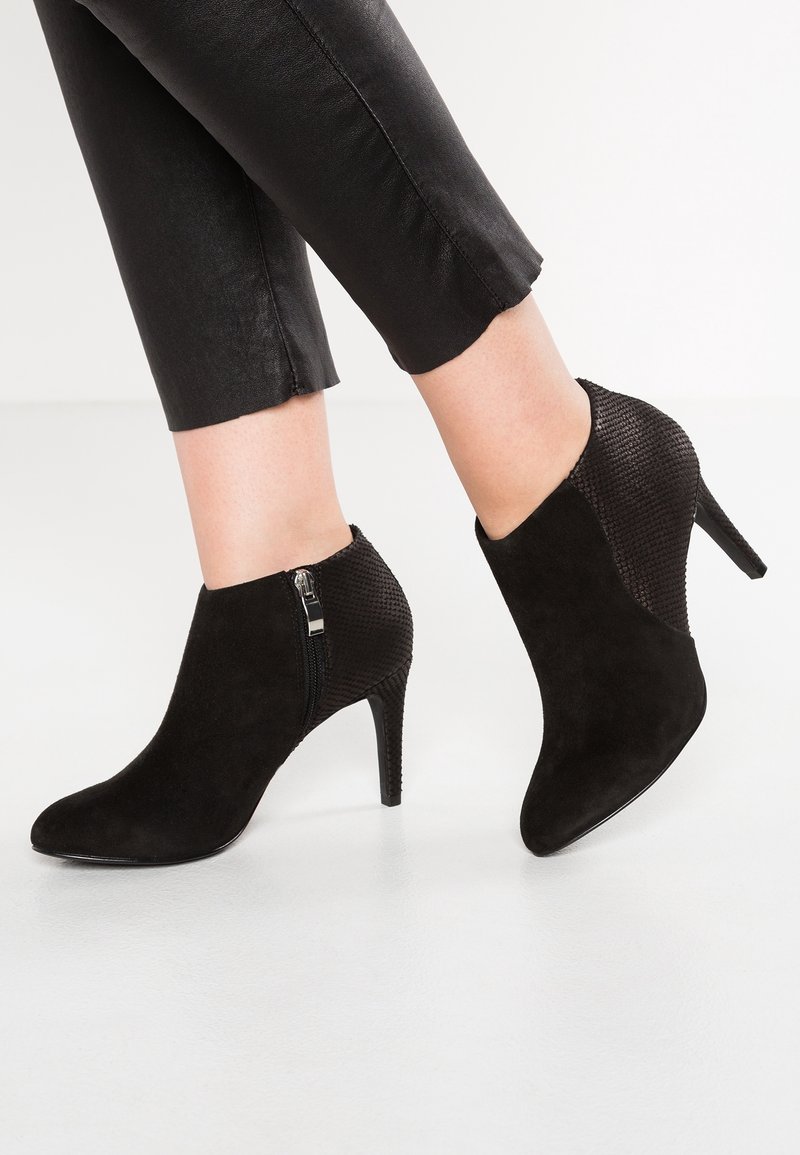 Stivaletti neri alla caviglia con punta affilata, materiale in suede, pannello posteriore testurizzato e zip laterale. Il tacco a stiletto aggiunge altezza.