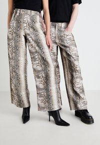 Pantaloni a gamba larga con motivo a pelle di serpente in tonalità beige e marrone, realizzati in tessuto morbido. Comprendono tasche e un design a vita alta.