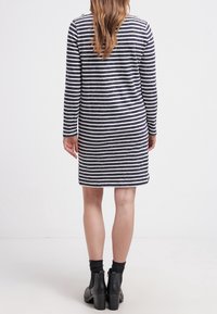 Robe rayée à manches longues en bleu marine et blanc. Coupe décontractée, longueur genoux, fabriquée en tissu doux. Portée avec des bottines noires et des chaussettes.