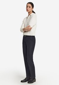 Vit stickad tröja med avslappnad krage, i kombination med mörkblå tapered byxor och svarta loafers. Enkel, modern design med släta texturer.