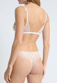 Set di reggiseno in pizzo e perizoma in beige chiaro. Caratterizzato da delicati motivi floreali, spalline regolabili e chiusura a gancio nella parte posteriore per una vestibilità sicura.
