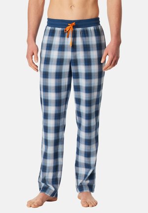 Mand iført blå, hvide og sorte ternede pyjamasbukser med navy taljebånd og orange snor, stående barfodet på hvid baggrund.