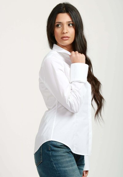 Camicia bianca a maniche lunghe, taglio su misura, con colletto aperto e polsini, abbinata a jeans blu. Tessuto liscio, design classico.