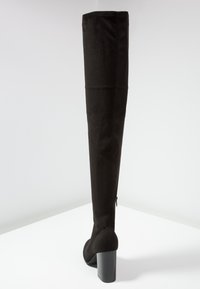 Botte noire cuissarde en matériau doux et texturé, avec un haut talon épais et un petit détail de fermeture éclair à l'arrière. Finition lisse dans l'ensemble.