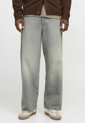 Jean baggy vert clair avec un délavage usé, présentant un design à jambe droite, associé à des baskets beiges et un cardigan marron.