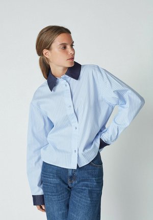 Light blue striped button-up shirt with a dark blue collar, long sleeves, and a relaxed fit, paired with blue jeans.