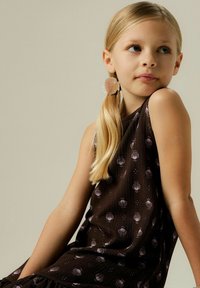 Robe marron foncé avec des accents en forme de coquillage, fabriquée en tissu texturé. Le modèle a une queue de cheval blonde claire et porte une boucle d'oreille en forme de coquillage.