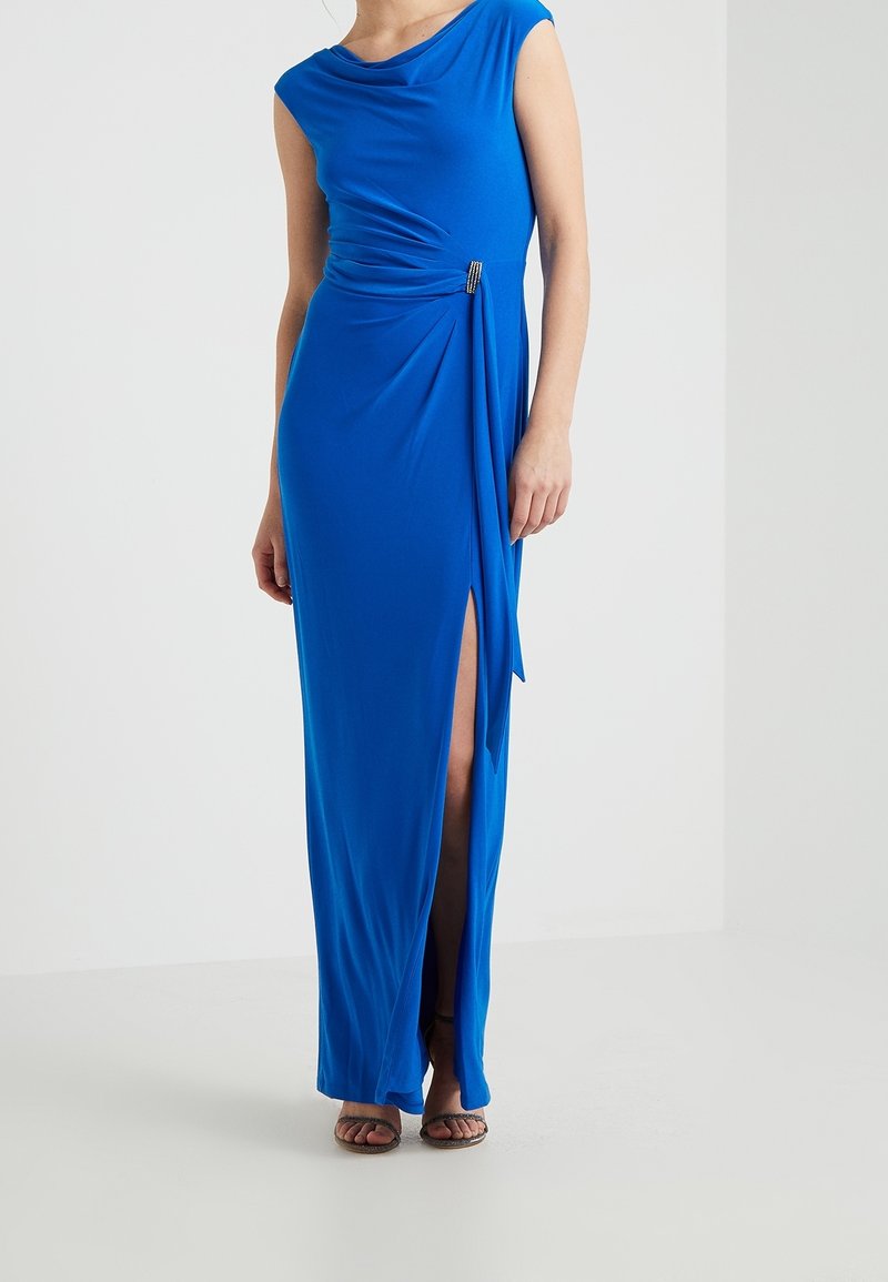 Long, blue dress with a draped neckline, side slit, and gathered detail at the waist featuring a decorative accent for added flair.