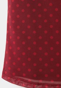 Tissu rouge transparent avec des pois rouges foncés régulièrement espacés et des coutures visibles le long de l'ourlet inférieur.