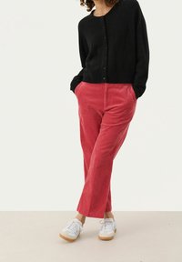 Svart knäpp cardigan över röda kordflosbyxor med rak benform. Kombinerad med vita sneakers med gummisula.