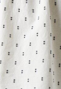 Tissu blanc avec de petits points noirs brodés, espacés régulièrement en paires, formant un motif subtilement pointillé.