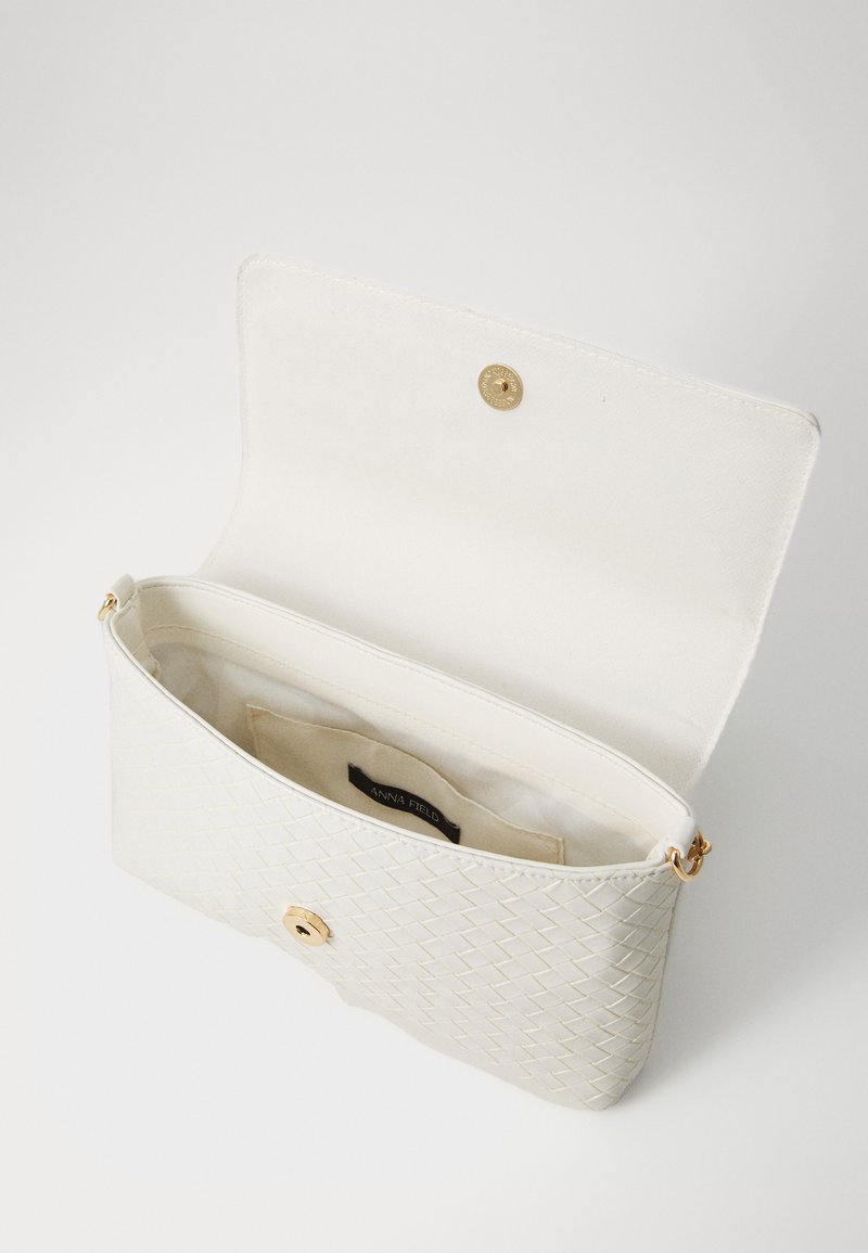 Bolso de mano de patrón tejido en color blanco con un cierre a presión dorado. El interior cuenta con un forro beige y una etiqueta. Textura suave y forma compacta.
