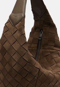 Brązowa torebka z tkanego zamszu ze srebrnym zamkiem i skórzaną naszywką z napisem „LIEBESKIND BERLIN” na pasku.