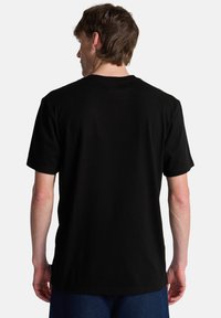 Μαύρο βαμβακερό t-shirt με στρογγυλή λαιμόκοψη, κοντά μανίκια και απλό πίσω σχέδιο. Διαθέτει ίσια κοπή και μαλακή υφή.