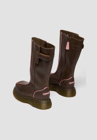 Pruunid nahast keskmise säärega saapad roosa äärega, külje tõmblukuga, rihma detailiga, paksud läbipaistvast kummist tallad ja oranži õmblusega valgel taustal.