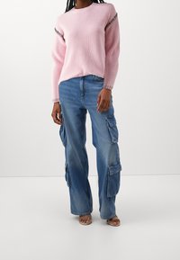 Ljusrosa ribbad stickad tröja med kontrasterande svart sömnad, matchad med lösa blå cargojeans med flera sidofickor.