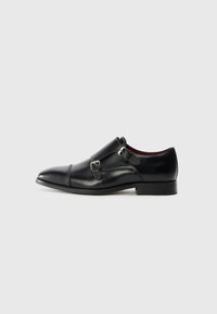 Schwarze Lederdressschuhe mit spitzem Zeh, doppelten Schnallenakzenten, glatter Textur und flacher Sohle. Besitzen ein dezentes, geschwungenes Design.