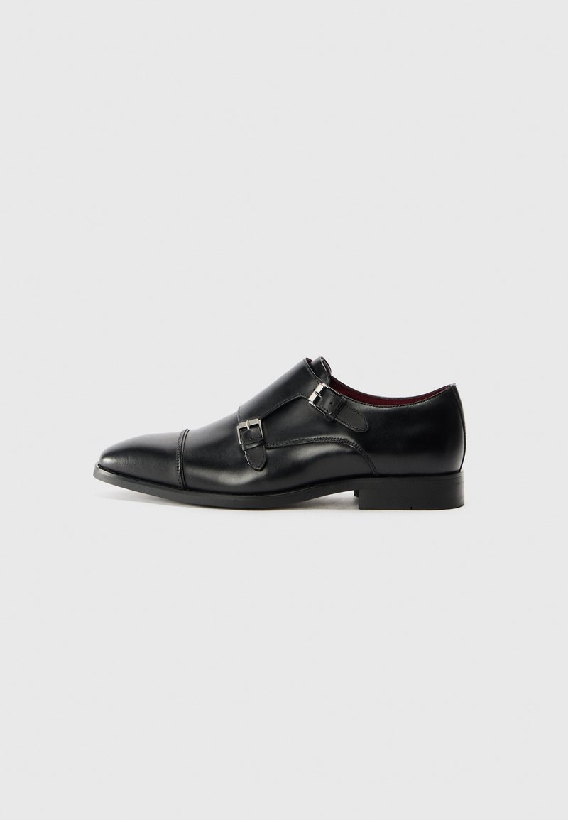 Schwarze Lederdressschuhe mit spitzem Zeh, doppelten Schnallenakzenten, glatter Textur und flacher Sohle. Besitzen ein dezentes, geschwungenes Design.