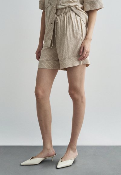 Shorts beige à motif avec une taille élastique et des poches latérales, associés à des mules blanches à bouts pointus. Texture de tissu lisse.