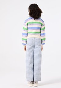 Multikleurige gestreepte trui met pastelgroene, blauwe en roomkleurige tinten; high-waisted lichte spijkerbroek met textuurpatroon; witte sneakers.