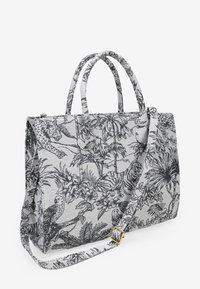 Bolso de tela gris con estampado botánico y de animales en negro, dos asas superiores y una correa de hombro desmontable con herrajes dorados.