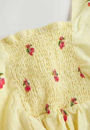 Gelbes Baumwollkleid mit gerafftem Oberteil und rosafarbener Kirschstickerei; leichter Stoff mit weicher Textur und fließendem Rock.