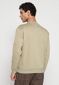 Khaki sweatshirt met een ronde halslijn en geribde boorden. Voorzien van een schouderpatch, getoond van achteren, met een gladde textuur.