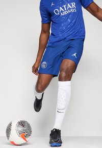 Blå sportstrøje med "QATAR AIRWAYS" logo, blå shorts med struktureret mønster, sorte fodboldstøvler, hvide sokker og en mønstrede fodbold.