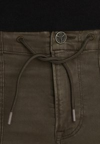 Pantalons en coton vert olive avec une taille à cordon, dotés d'un bouton en métal avec une marque et d'une texture subtile sur le tissu.