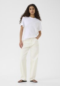 T-shirt bianco in cotone con vestibilità comoda, abbinato a pantaloni crema a gamba larga. Il modello indossa ciabatte nere. Design semplice e casual senza motivi.