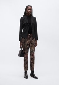 Blazer nero aderente, maglione nero a coste, pantaloni a fantasia floreale in tonalità scure, stivaletti neri e una piccola borsa nera.