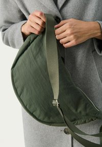Borsa a spalla verde trapuntata con forma curva, dotata di tracolla staccabile e hardware in argento. Tessuto testurizzato con finitura opaca.