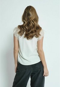 Cremefarvet bluse med blondekant på korte ærmer, parret med mørke, vide jeans. Stoffet ser glat ud med en afslappet pasform.