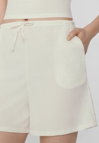 Pantaloni corti bianchi con texture, dotati di vita elastica e cordino. Presentano tasche laterali e una vestibilità comoda, che termina sopra il ginocchio.