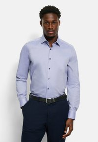 Hellblaues langärmliges Hemd mit dezentem Karomuster, Kentkragen und blauen Knöpfen, getragen mit dunklen Hosen und einem schwarzen Gürtel.