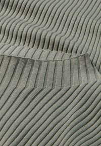 Rippstrickstoff in gedämpftem Salbeigrün, mit gleichmäßigen vertikalen Linien und einer weichen Textur, die ein gefaltetes Kanten-Detail zeigt.