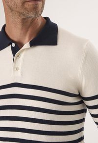 Herren-Polohemd in Creme mit navyfarbenen horizontalen Streifen. Verfügt über einen kontrastierenden navyfarbenen Kragen und eine Drei-Knopf-Verschluss, hergestellt aus strukturiertem Strickstoff.