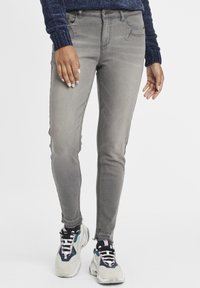 Szürke skinny farmer közép-derékrésszel, ötpockets kivitelben, enyhén kopott hatással. Vastag talpú sportcipőkkel párosítva, kék-szürke dizájnnal.