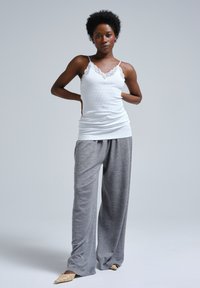 Vit ribbad linne med spetskant, ihop med löst sittande gråbyxor. Modellen står framför en neutral bakgrund och visar upp outfitens flöde.