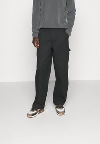 Person wearing black wide-leg pants, gray long-sleeve top, and white, brown, and pink sneakers standing against a plain background.