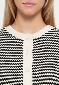 Cardigan a righe bianco e nero con scollo tondo, realizzato in tessuto a maglia, caratterizzato da tre bottoni sulla parte anteriore.