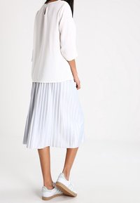 White blouse with three-quarter sleeves and a keyhole back, paired with a pleated light blue skirt and white sneakers with mint accents.