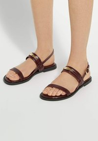 Bruine leren sandalen met meerdere dunne banden over de voet, platte zool en verstelbare gesp. Heeft een subtiele metalen accent.