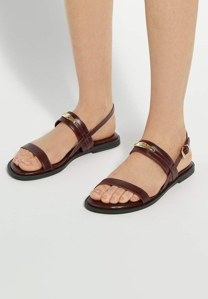 Bruine leren sandalen met meerdere dunne banden over de voet, platte zool en verstelbare gesp. Heeft een subtiele metalen accent.