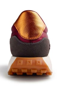 Sneaker bordeaux con tacchetti in pelle arancione lucido, dettagli in suede grigio e suola in tessuto color sabbia; presenta cuciture a contrasto e un design stratificato.