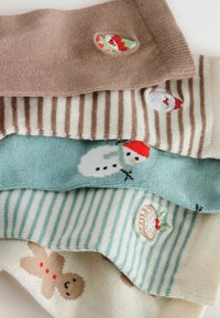 Sosso in maglia a tema natalizio in vari colori: marrone con un albero, crema a righe con Babbo Natale, verde con un pupazzo di neve, crema con un uomo di pan di zenzero.